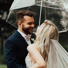 Bride and Groom standing under clear umbrella. 